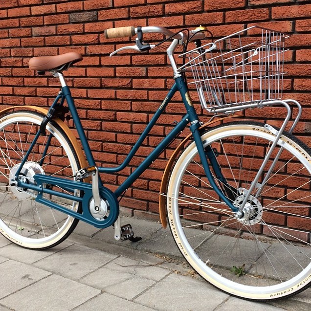 Roetz Road+ Ladies Elektrische fiets in de kleur Matt Ocean blue met als achtergrond een bakstenen muur
