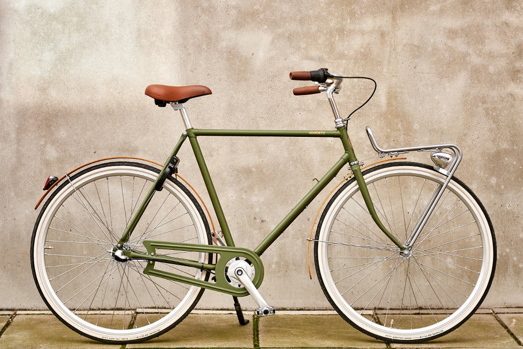 Roetz Road Men in de kleur Moss Green met een betonnen achtergrond.