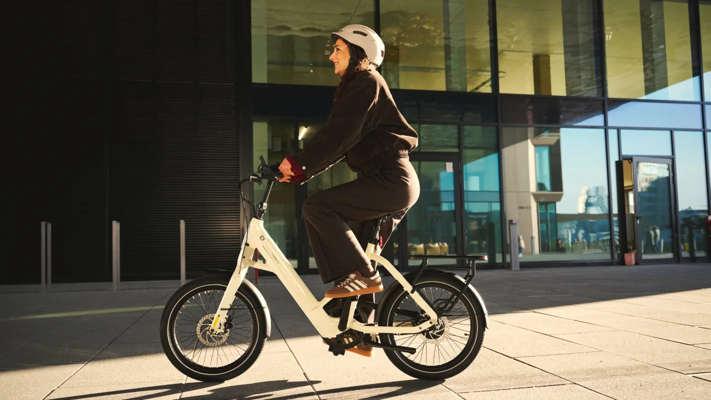 Een vrouw fietst in de zon op een TENWAYS CGO Compact langs een glazen gebouw